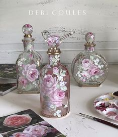 three glass bottles with pink flowers painted on them sitting on a table next to other items