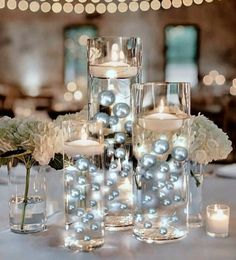 candles and flowers are arranged in glass vases on a table with lights behind them