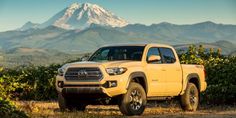 a yellow toyota truck parked in front of a mountain with snow capped peaks behind it