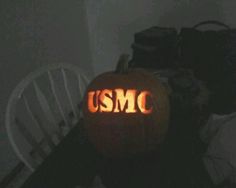 a pumpkin with the word usmc carved into it sitting on a chair in a dark room