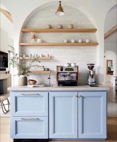 a kitchen with blue cabinets and shelves filled with coffee pots on top of the counter