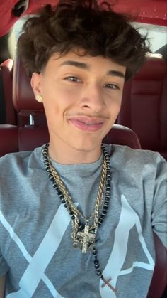 a young man sitting in the back seat of a car with a necklace on his neck