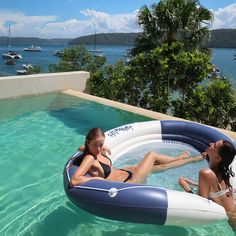 two girls are in the pool with an inflatable raft