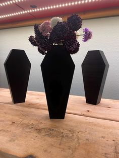 three black vases with flowers in them sitting on a wooden table next to a mirror