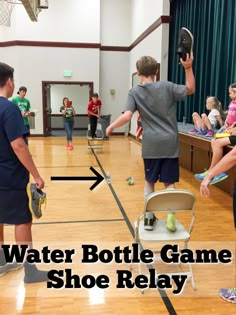 two young boys are playing water bottle game in a gym with other children watching them