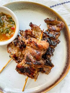 a white plate topped with skewered meat next to a bowl of soup