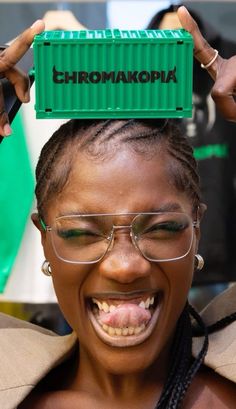 a woman wearing glasses holding up a green box over her head with the word chromakopia on it