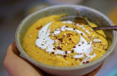 a hand holding a small bowl filled with yellow and white liquid, topped with whipped cream