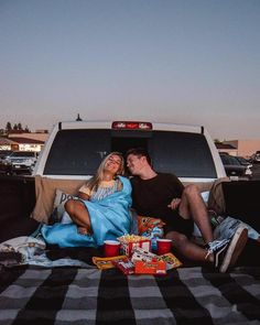 a man and woman sitting in the back of a pickup truck with food on the bed