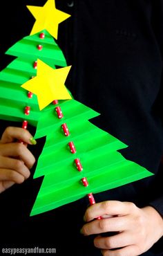 a person holding a paper christmas tree with red and yellow stars on it, made from construction paper