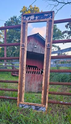 an old wooden mirror sitting on top of a grass covered field next to a fence