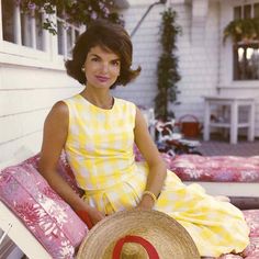 a woman sitting on top of a bed wearing a yellow and white checkered dress