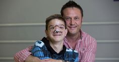 a man with his face painted to look like a football player is hugged by a young boy