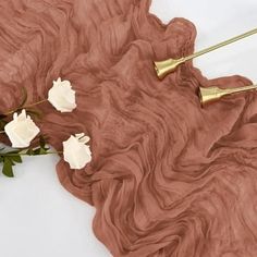 some white flowers and gold hair pins on a brown cloth with pink waves in the background