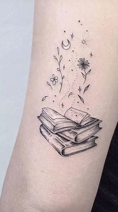 a woman's arm with a tattoo on it that has an open book and flowers coming out of it