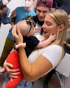 a woman holding a baby in her arms while wearing a face mask and standing next to other people