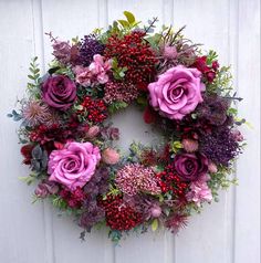 a wreath with purple flowers and greenery hanging on a white door, decorated with berries