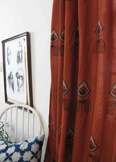 an orange curtain with black and white drawings on it next to a chair in front of a mirror