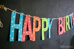 a happy birthday banner hanging from a string on a chalkboard wall with polka dots