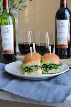 two sandwiches on a plate with wine bottles and glasses in the backgroung