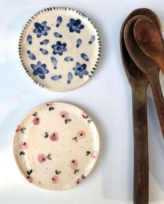 three plates and two wooden spoons on a white surface with blue flowers painted on them