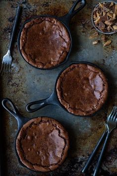 three chocolate pies sitting on top of a pan next to forks and spoons