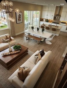 an aerial view of a living room and kitchen area with hardwood floors, white couches, large windows, and wooden coffee table