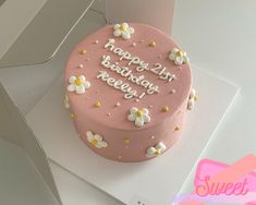 a pink birthday cake sitting on top of a white table next to an open box