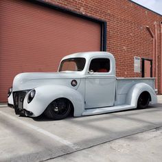 an old white truck parked in front of a brick building next to a garage door