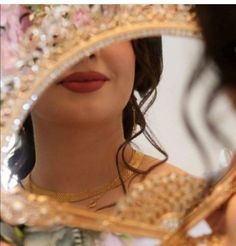 a woman is looking in the mirror while wearing a bridal dress and holding a gold necklace