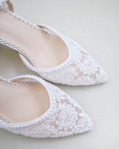 a pair of white shoes with lace and pearls on the toes, sitting on a table