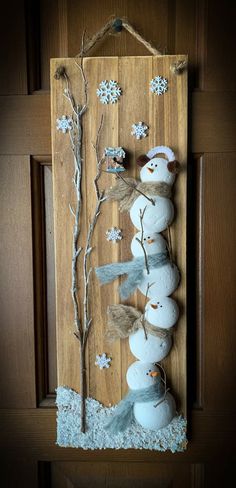 a snowman made out of rocks and branches on a wooden door hanger with white balls