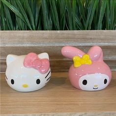 two hello kitty figurines sitting on top of a wooden table next to green plants