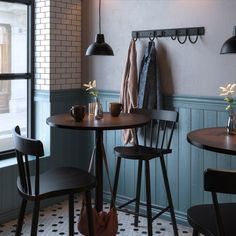 two wooden tables and chairs in a room with blue painted walls, white tile flooring and coat rack on the wall