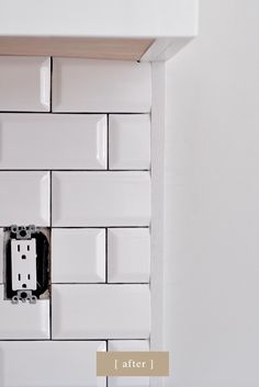 an electrical outlet in the wall with white tiles on it and a light switch box