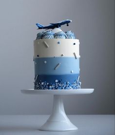 a blue and white cake with an airplane decoration on top is sitting on a pedestal