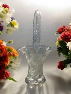 there is a glass vase with a handle on it and flowers in the back ground