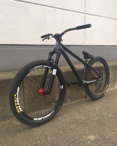 a black bike parked on the side of a building next to a curb with no one around it