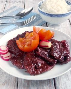 a white plate topped with meat and veggies next to a bowl of rice