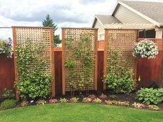 a wooden fence with flowers growing on it next to a tree and grass in front of a house