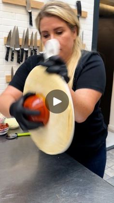 a woman in black shirt and gloves holding a pizza doughnut on top of a counter