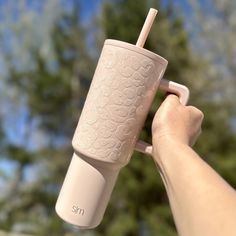 a person holding up a pink cup with a straw in it's mouth and trees in the background