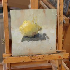 an easel with a painting on it and a yellow flower sitting on top of it