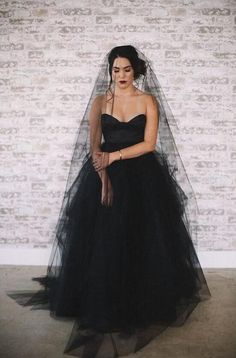 a woman wearing a black dress and veil standing in front of a white brick wall