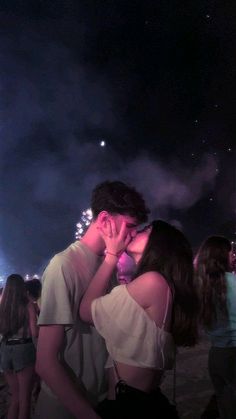 a man and woman kissing in front of fireworks on the beach with people watching them