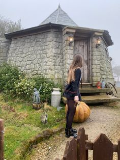 a woman sitting on top of a wooden bench next to a stone building and pumpkins