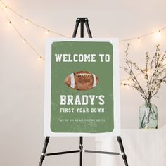 a welcome sign with a football on it in front of a white wall and string lights