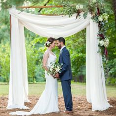 a bride and groom are standing under an arch with white draping on it