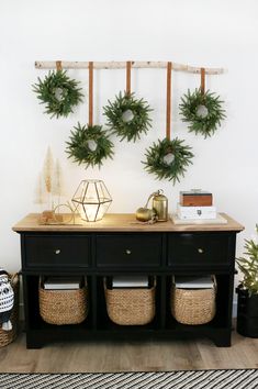 two wreaths are hanging on the wall above a black dresser with baskets underneath it