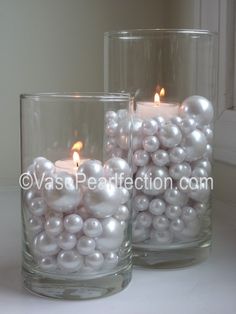 two glass vases filled with white pearls and lit candles on a window sill